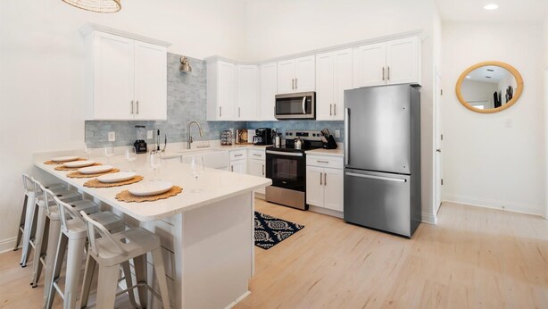 Una cocina moderna con armarios blancos, electrodomésticos de acero inoxidable y una isla central con taburetes de bar.