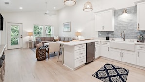 Une cuisine moderne avec des meubles blancs, un îlot central, des luminaires suspendus et une vue sur l’extérieur.