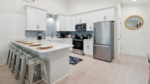 Une cuisine moderne avec des meubles blancs, des appareils en acier inoxydable et un îlot central doté de tabourets de bar.