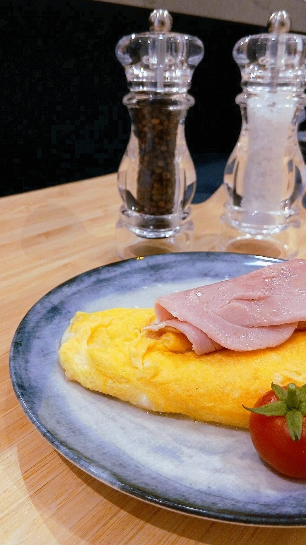 A plate with an omelette, ham, and a tomato on a ceramic plate.