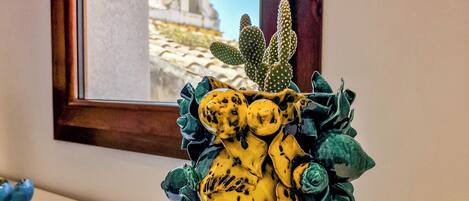A ceramic vase with a yellow and green design, placed on a white surface near a window.