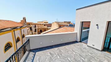 A rooftop terrace with a tiled floor, a metal railing, and a view of neighboring buildings.
