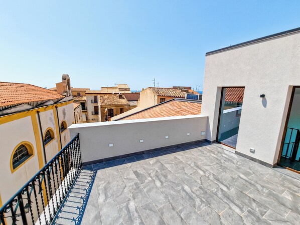 A rooftop terrace with a tiled floor, a metal railing, and a view of neighboring buildings. - Thaleia Dimora di Pregio (Cefalù)