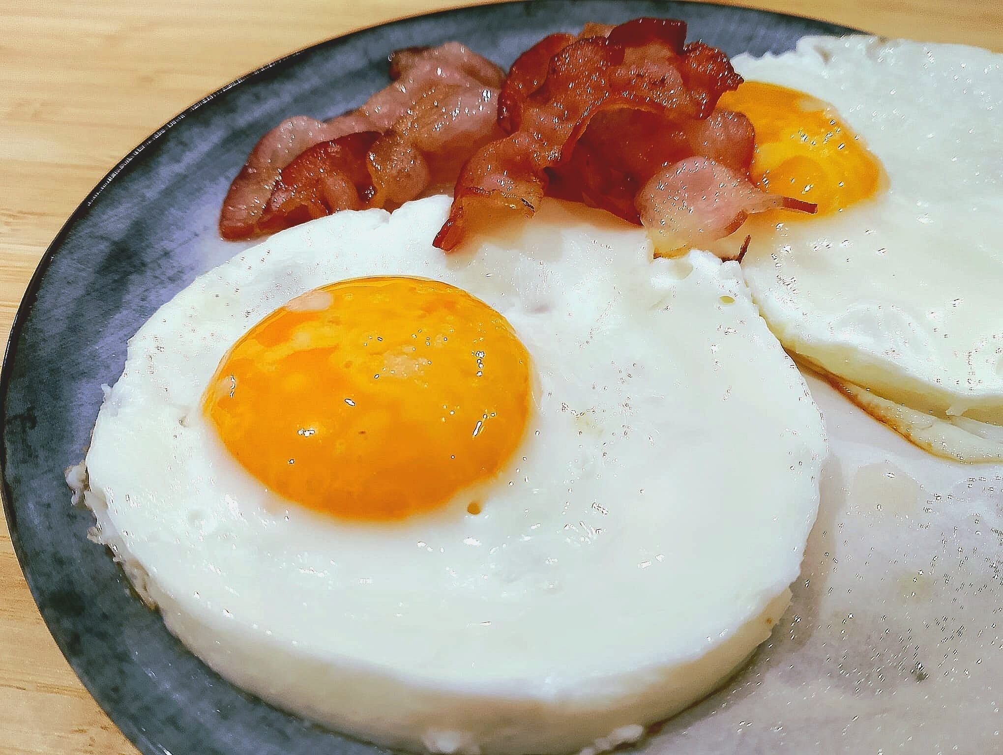 Un plato con dos huevos revueltos y tiras de tocino.