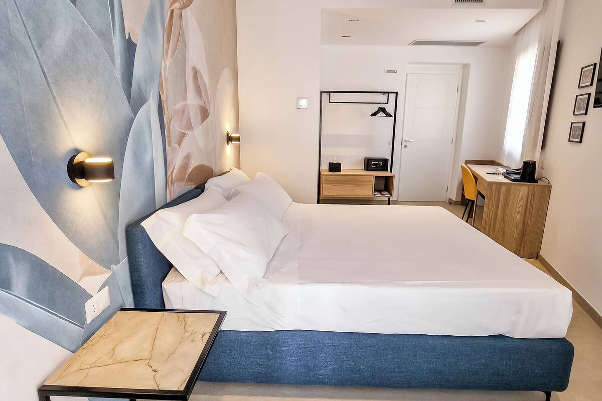 Une chambre d’hôtel moderne avec un grand lit, une table de chevet, une armoire et un bureau avec une chaise.
