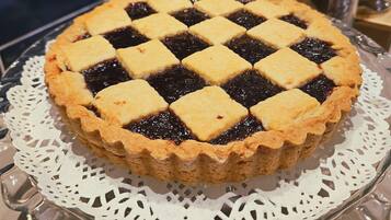 Une tarte recouverte d’une pâte en croisillons, présentée sur une assiette en verre ornée d’un chemin de table, le tout posé sur une table dont le mur est recouvert de carreaux.