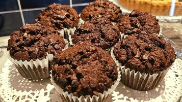 Bandeja de muffins de chocolate sobre un plato de vidrio con un mantel de encaje, en una cocina con salpicadero de azulejos.