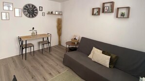 Un salon comprenant un canapé, une table à manger avec des chaises, une lampe suspendue et des tableaux encadrés accrochés aux murs.