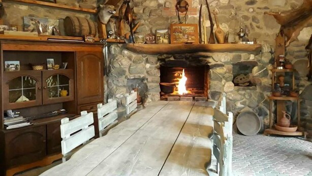 A rustic interior with a stone fireplace, wooden furniture, and various decorative items. - Safari House (Tbilisi)