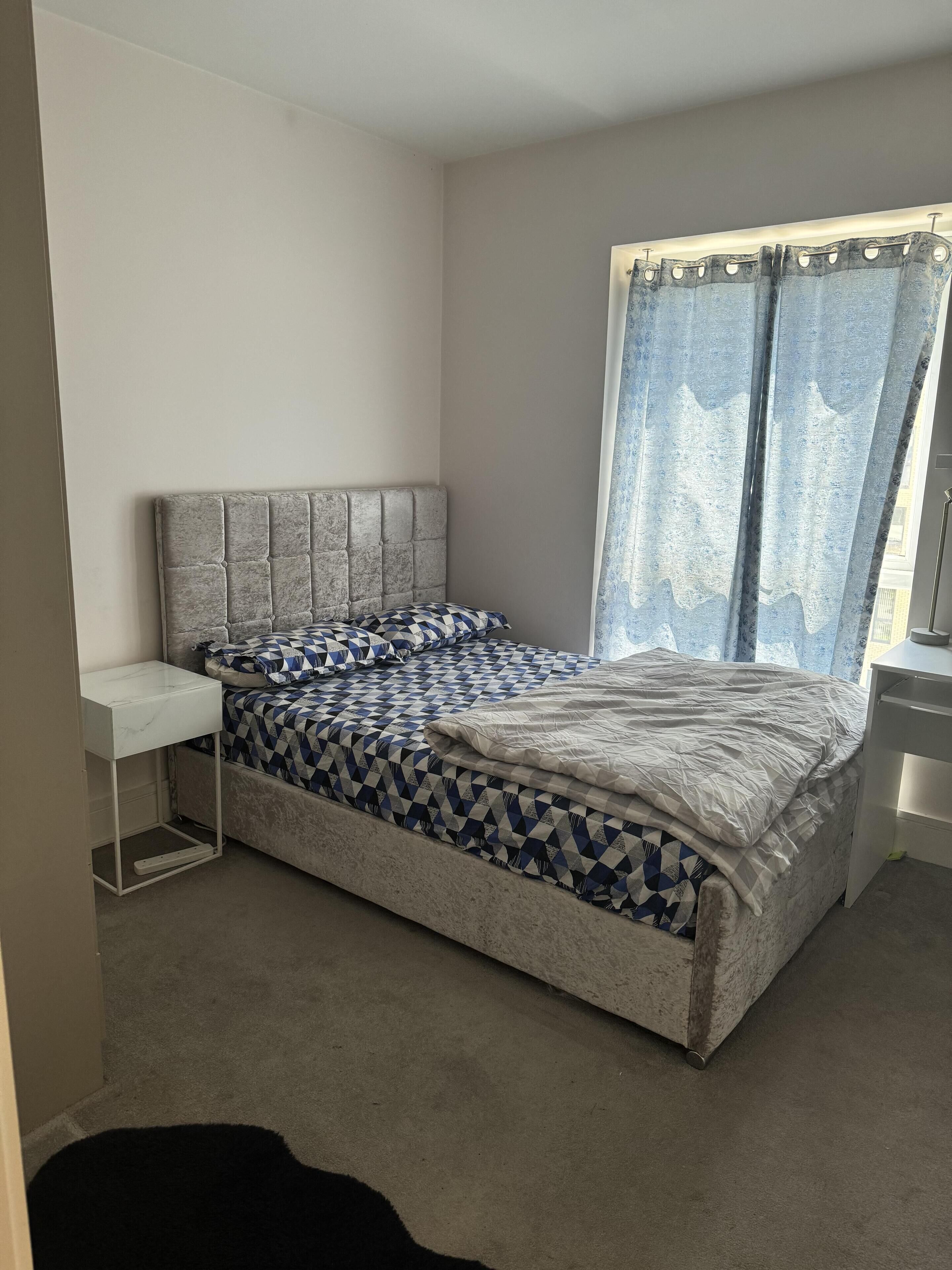 A bedroom with a bed, a bedside table, and a window with curtains.