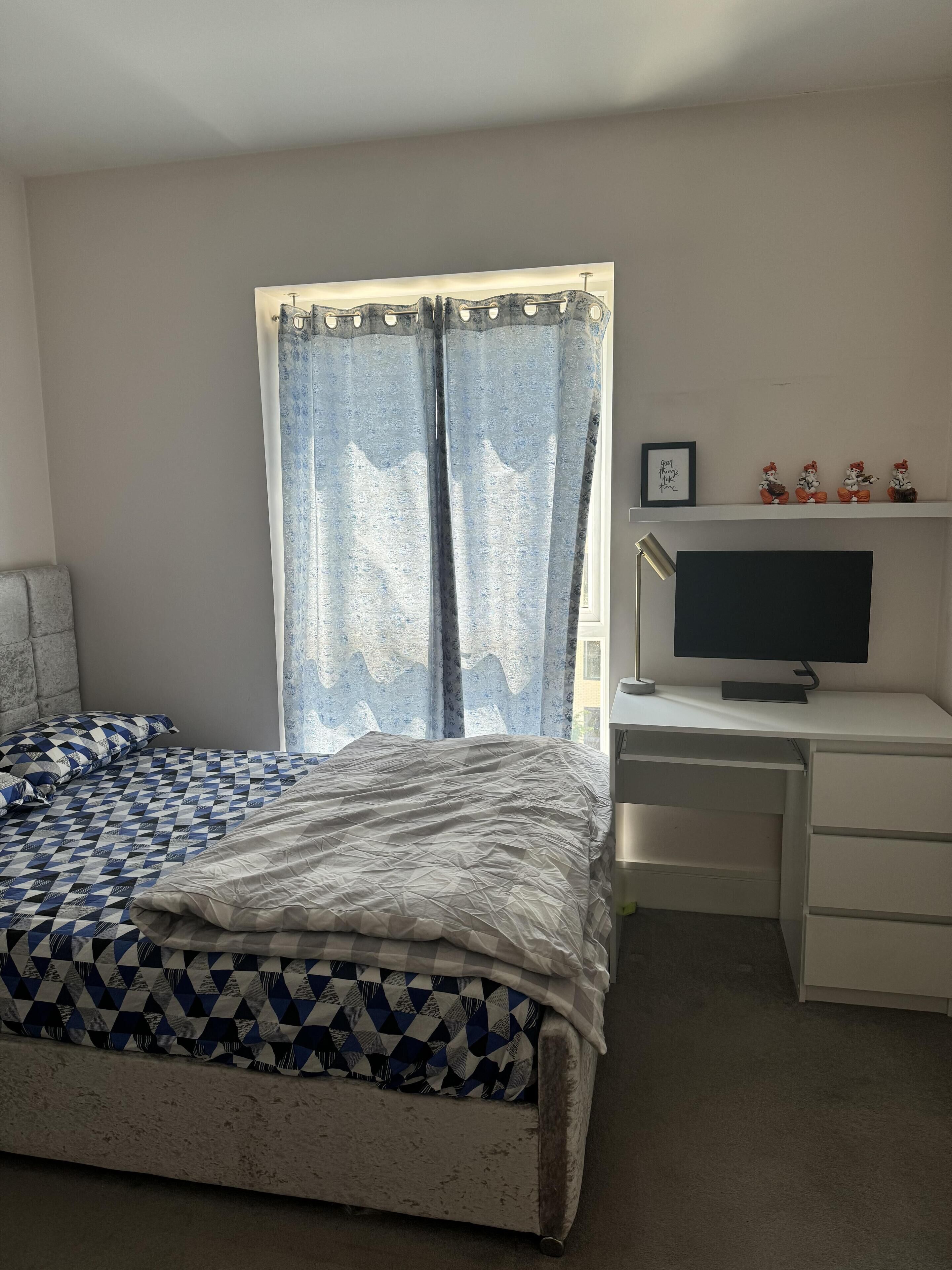 A bedroom with a bed, a desk with a computer, and a window with curtains.