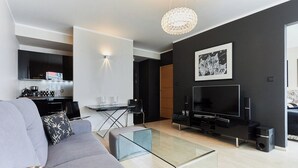 A modern living room with a grey sofa, a glass coffee table, a flat-screen TV, and a dining area with a small table and chairs. - Stella Baltic by Baltic Home (Swinoujscie)
