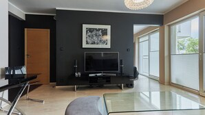 A modern living room with a flat-screen TV, a glass coffee table, and a large window offering a view of the outdoors. - Stella Baltic by Baltic Home (Swinoujscie)