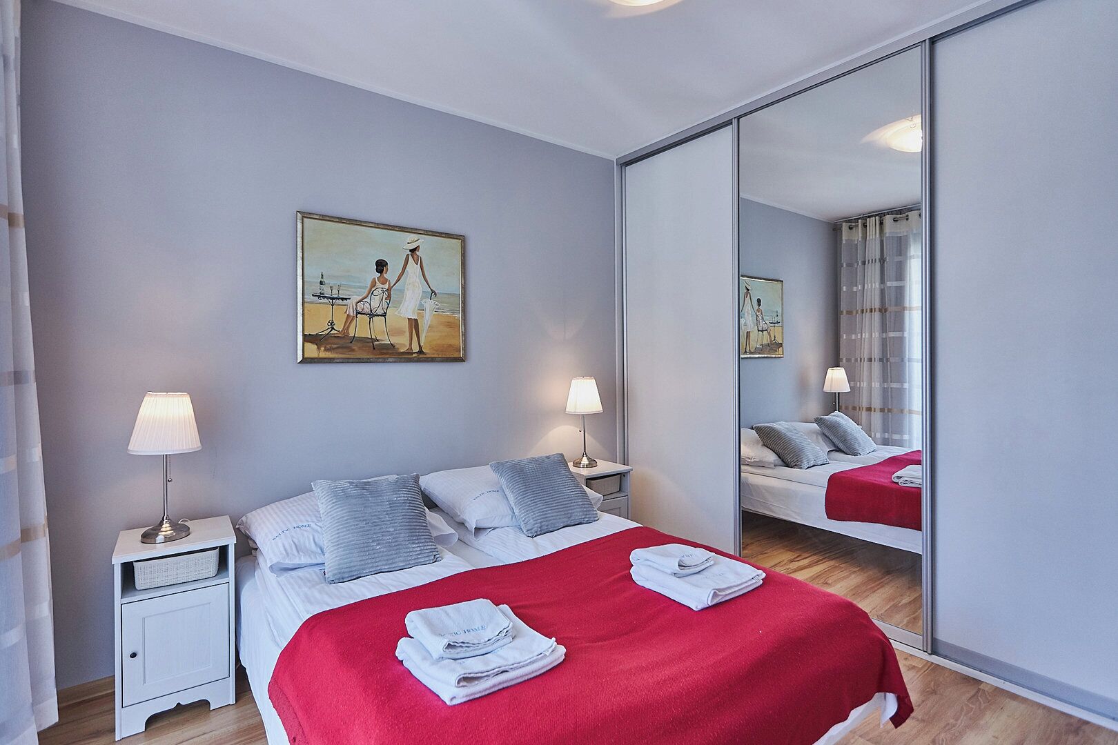Une chambre d’hôtel avec un lit, deux tables de chevet avec des lampes, un tableau au mur et un grand miroir qui reflète la pièce.