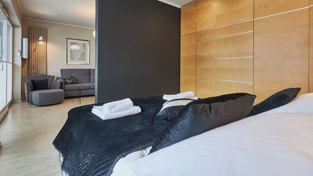 A modern hotel room with a large bed, a sofa, and a wooden wardrobe. - Stella Baltic by Baltic Home (Swinoujscie)