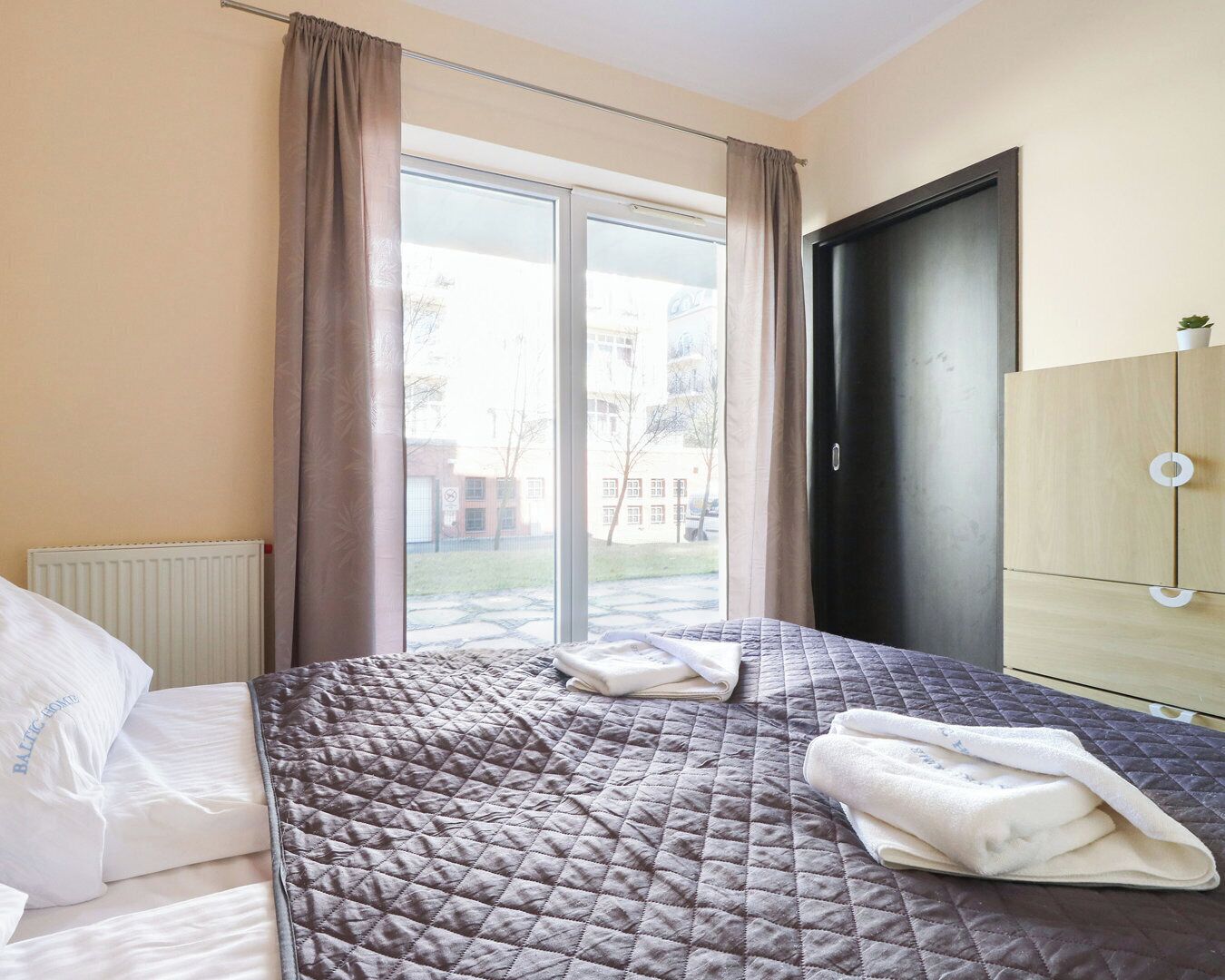 Une chambre d’hôtel avec un lit, un radiateur, une fenêtre avec des rideaux et une armoire.