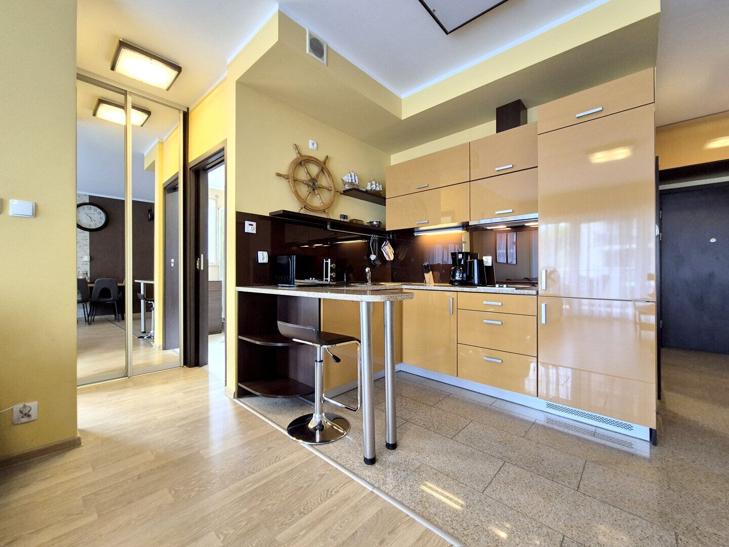 A modern kitchen with a central island, wooden cabinets, and a ship's wheel decoration.
