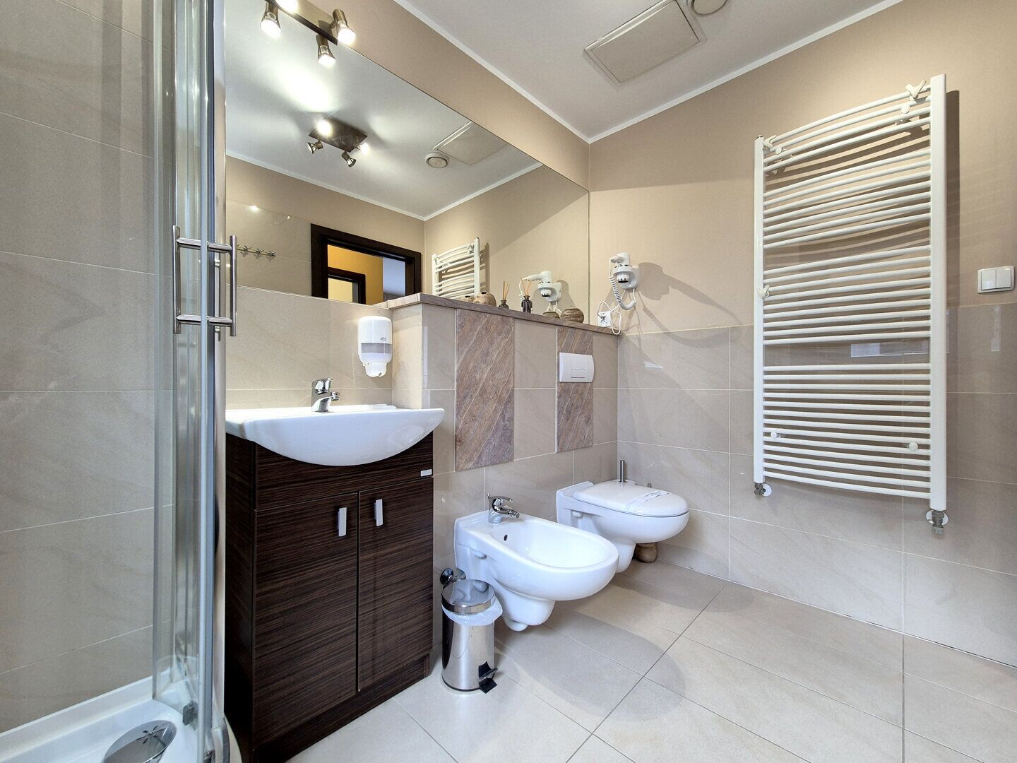 Un baño moderno con cabina de ducha de vidrio, un lavamanos grande, dos bidés y un perchero para toallas.