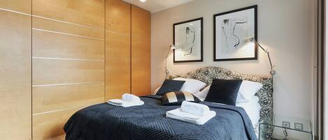 Un dormitorio moderno con una cama grande, un armario de madera y dos cuadros enmarcados en la pared.