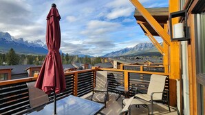 Ein Balkon mit Tisch und Stühlen, einem roten Sonnenschirm und Blick auf die Berge.