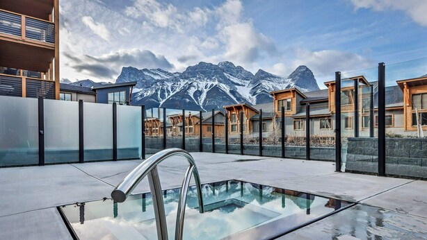 Ein Pool auf dem Dach mit Glasgeländer, moderne Gebäude und ein Berg im Hintergrund.