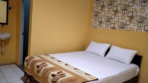 A hotel room with a bed, white pillows, a patterned bedspread, a wall-mounted sink, and a door with a window. - Hotel Mitra Kapuas Raya Sintang (Sintang)