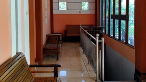 A corridor with wooden benches, a tiled floor, and large windows with a view of greenery. - Hotel Mitra Kapuas Raya Sintang (Sintang)