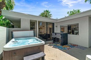 A modern outdoor hot tub area with a patio, seating, and a view of the interior. - Bamboo Bungalow (Palm Springs)