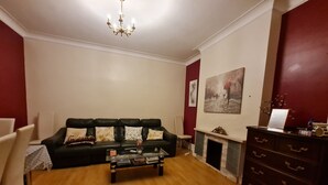 A living room with a black leather sofa, a coffee table, a fireplace, and a dresser. - House-sleeps4-parking-garden (London)