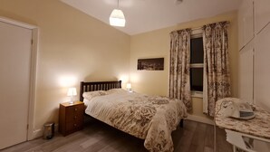 A bedroom with a bed, bedside tables, a desk, and a window with curtains. - House-sleeps4-parking-garden (London)