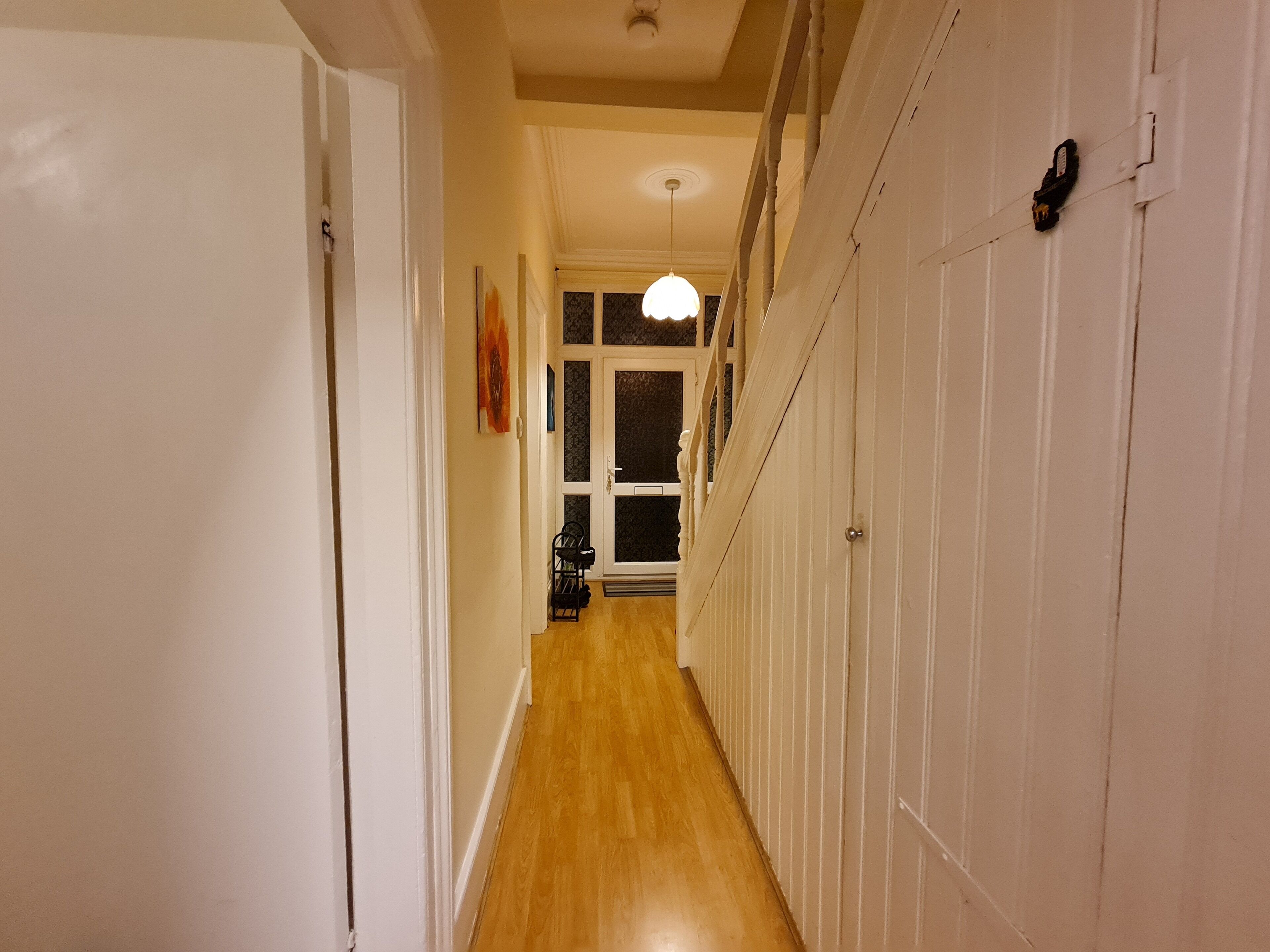 A hallway with a wooden floor, white walls, and a door at the end.