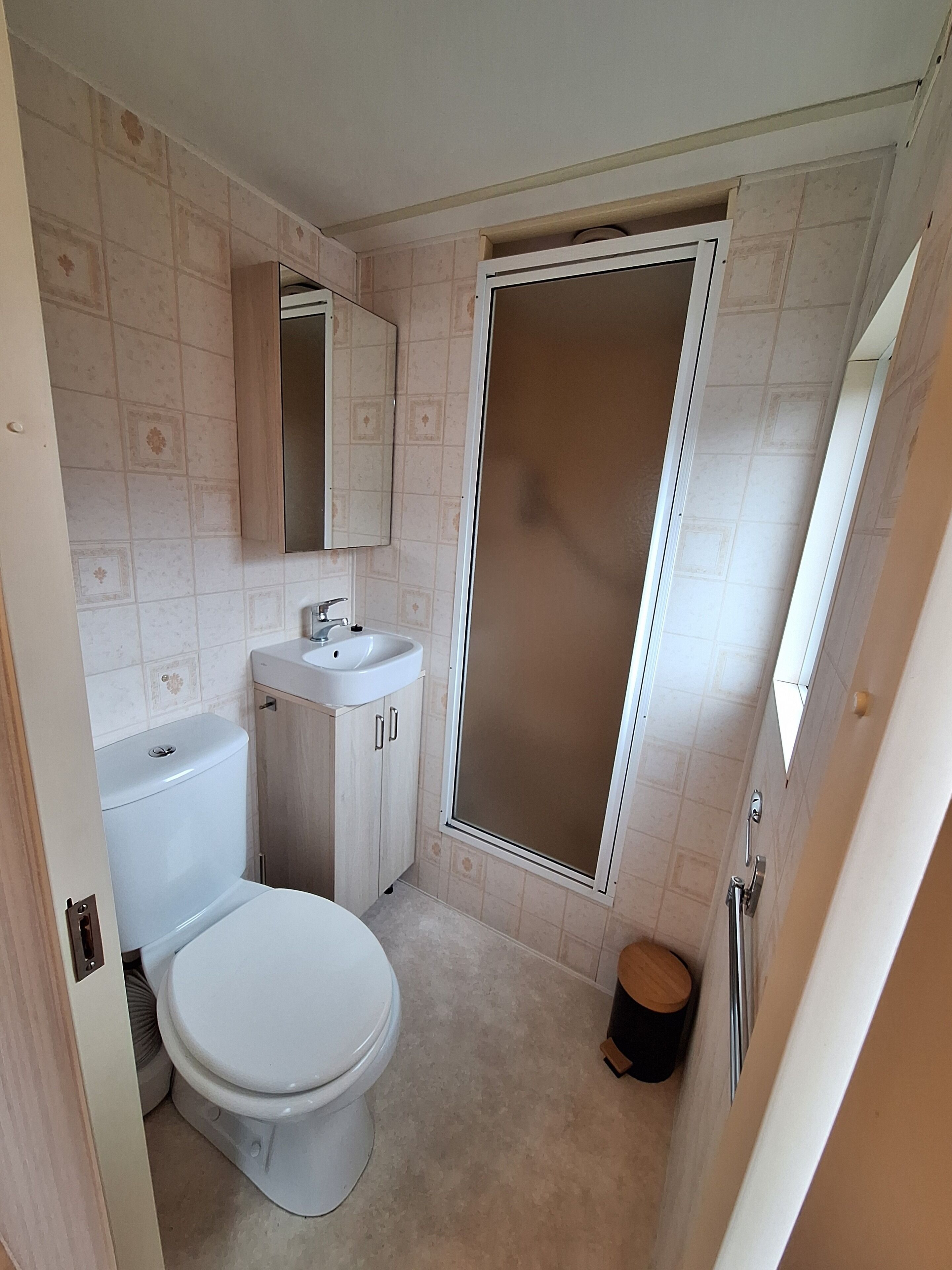 Baño con inodoro, lavabo, espejo y cabina de ducha.