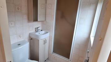 Baño con inodoro, lavabo, espejo y cabina de ducha.