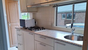A modern kitchen with white cabinets, a stainless steel sink, and a window overlooking a brick building. - Gezellige Ruime Stacaravan om Lekker tot Rust te Komen bij ons op de Camping (Burum)