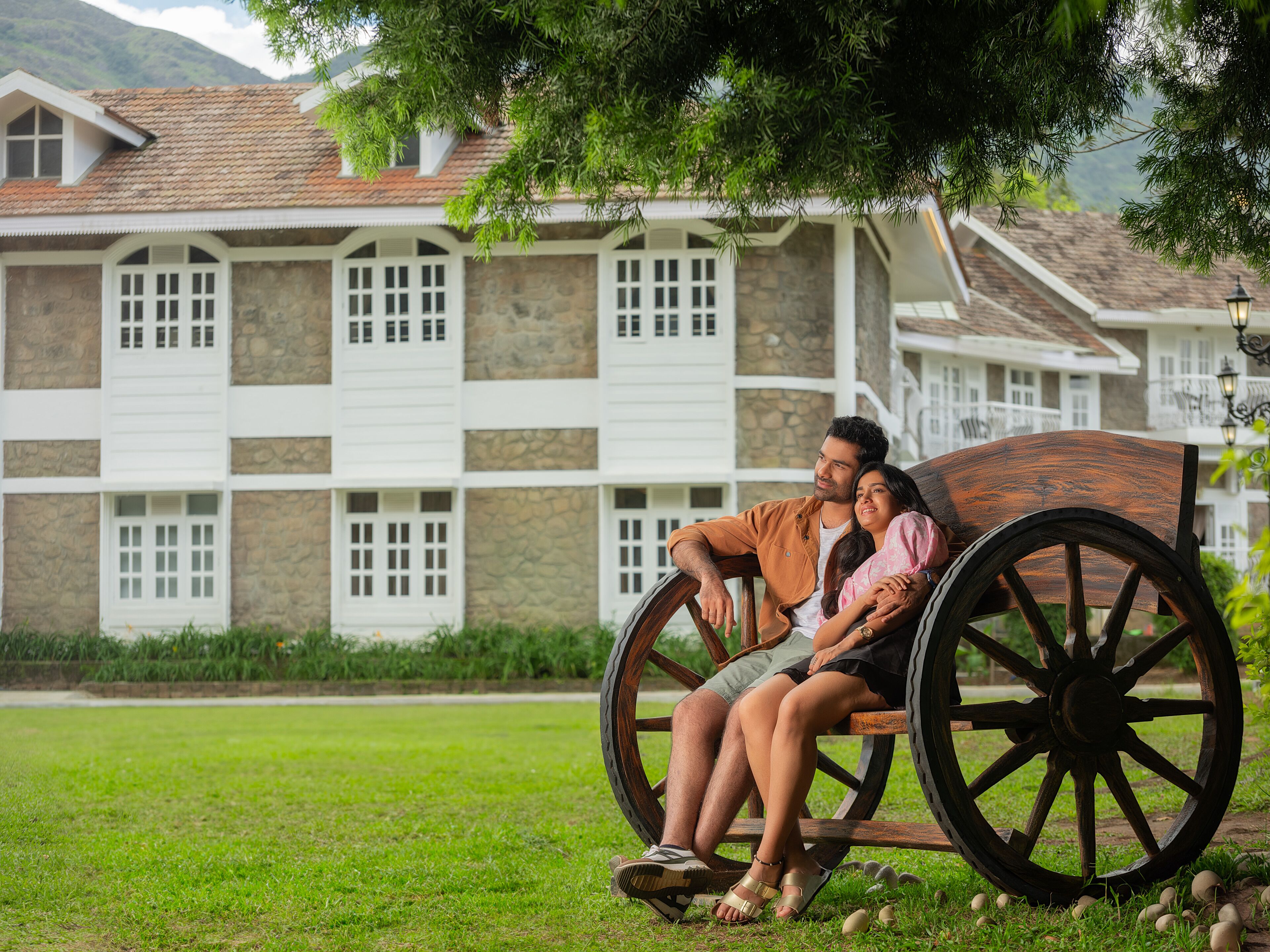 A couple sitting on a wooden bench with a stone building in the background.