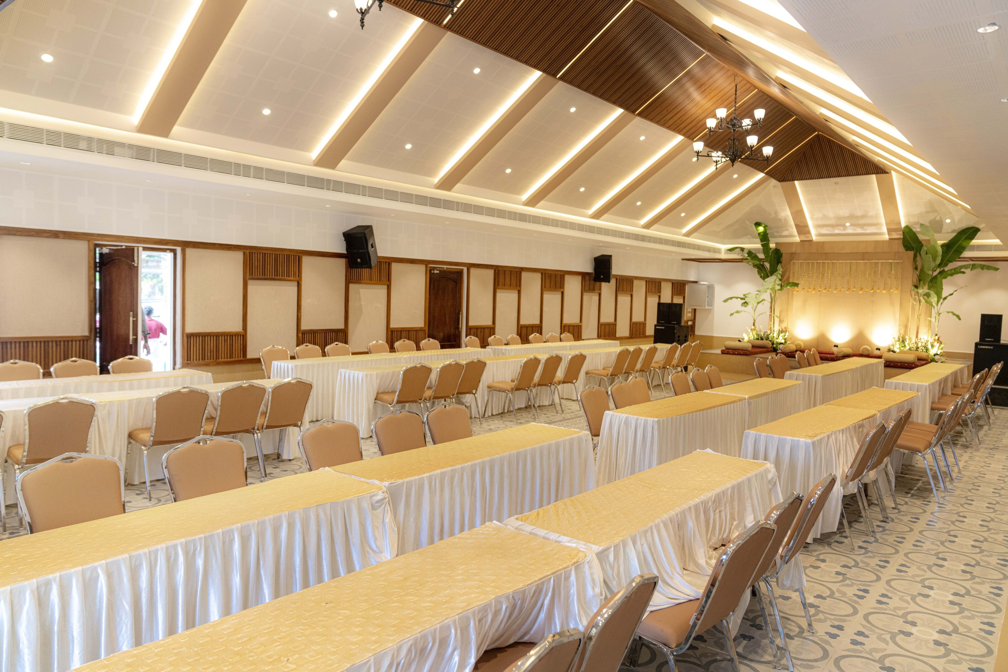 A banquet hall with long tables, chairs, and a high ceiling with lighting fixtures.