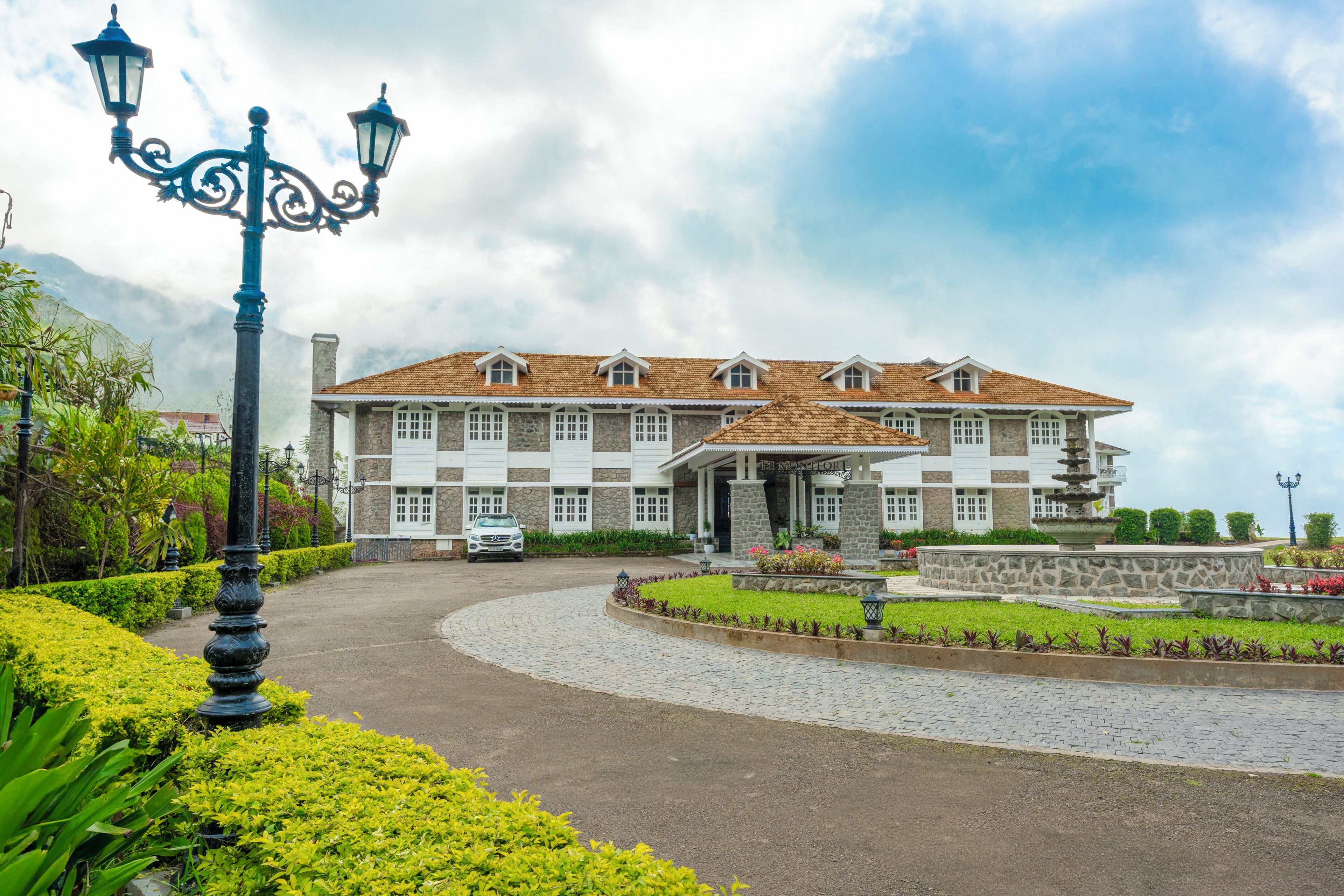 A large, multi-story building with a stone facade, a tiled roof, and a landscaped driveway.