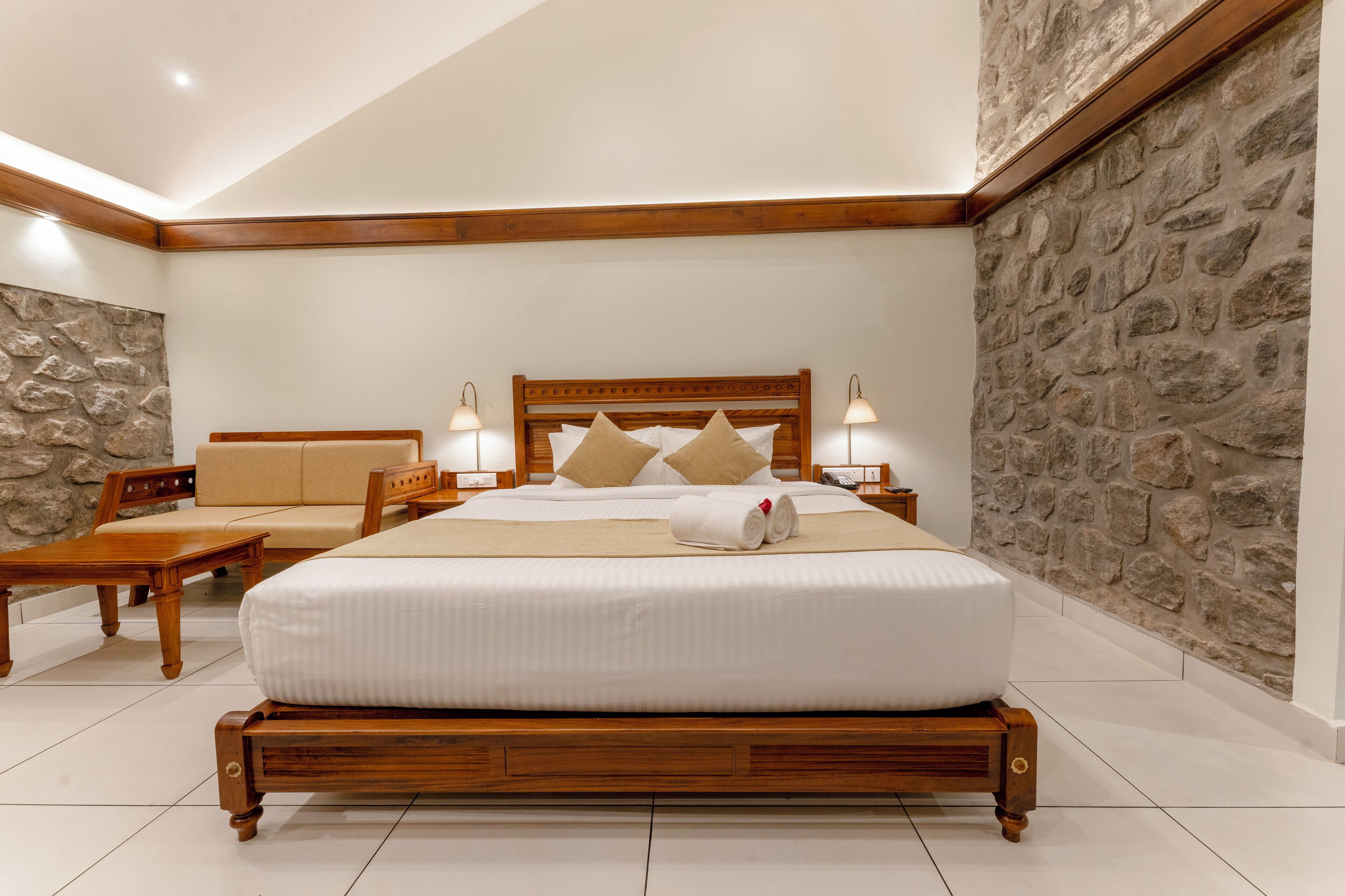 Un dormitorio ordenado con una cama de madera, un sofá y una pared de acento de piedra.
