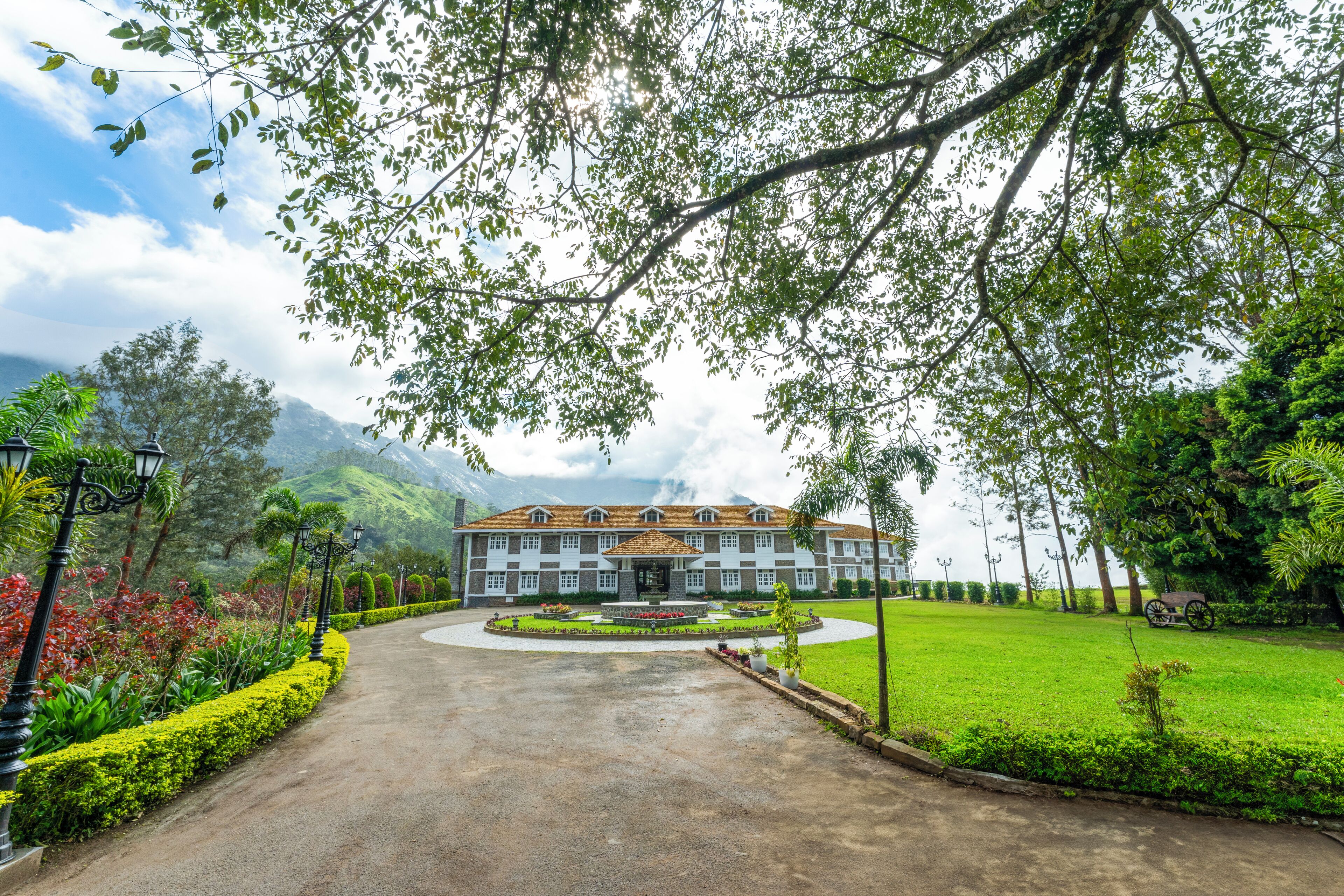 A large building with a symmetrical facade, surrounded by well-maintained gardens and a paved driveway leading to the entrance.