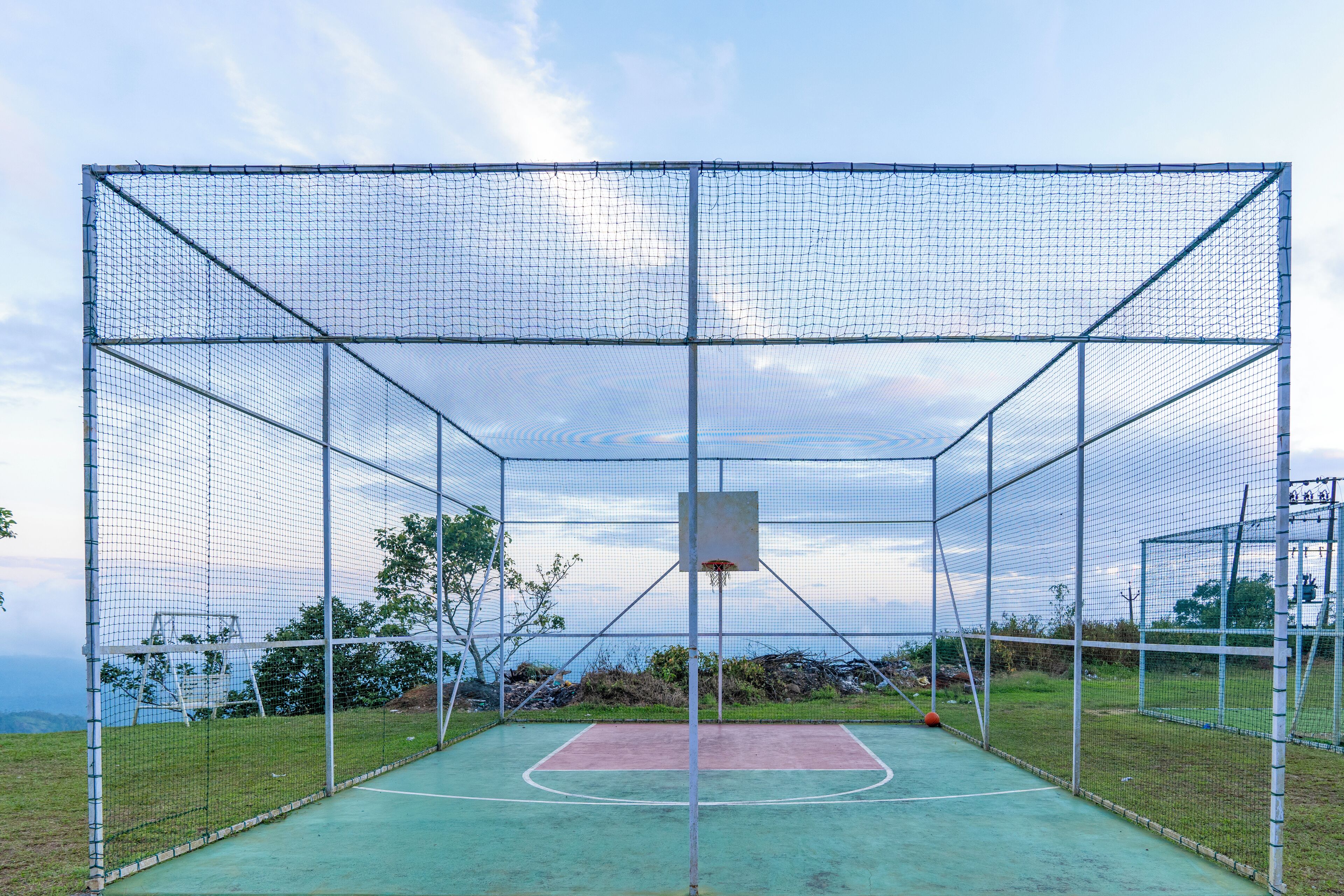 A basketball court enclosed by a netted structure with a basketball hoop in the center.