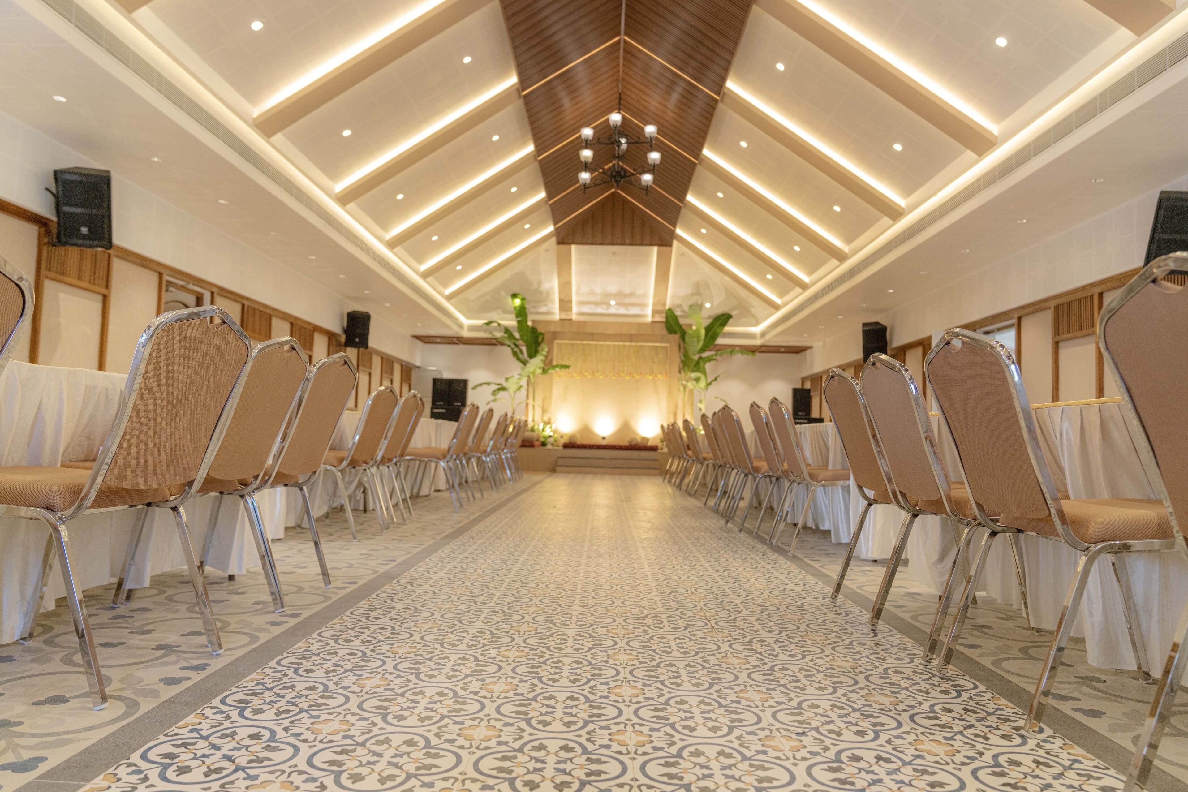 A long, narrow room with rows of chairs and tables, a patterned floor, and a high ceiling with recessed lighting.