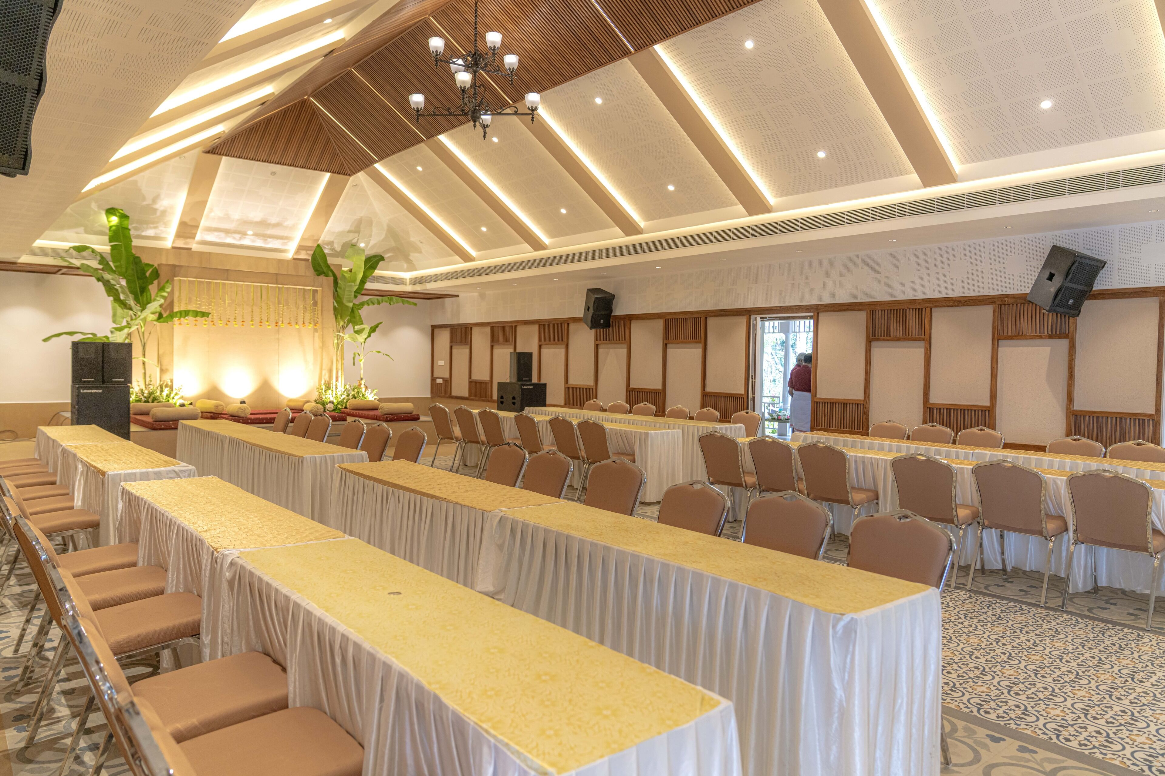 Una sala de conferències amb taules llargues, cadires i un sostre amb llistons de fusta i il·luminació empotrada.