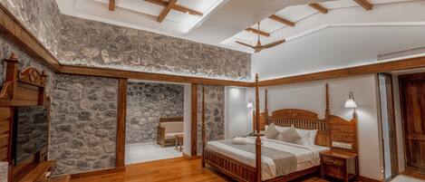 Un dormitorio con pared de piedra, vigas de madera en el techo y una cama con dosel, junto a una mesita de noche con lámpara.