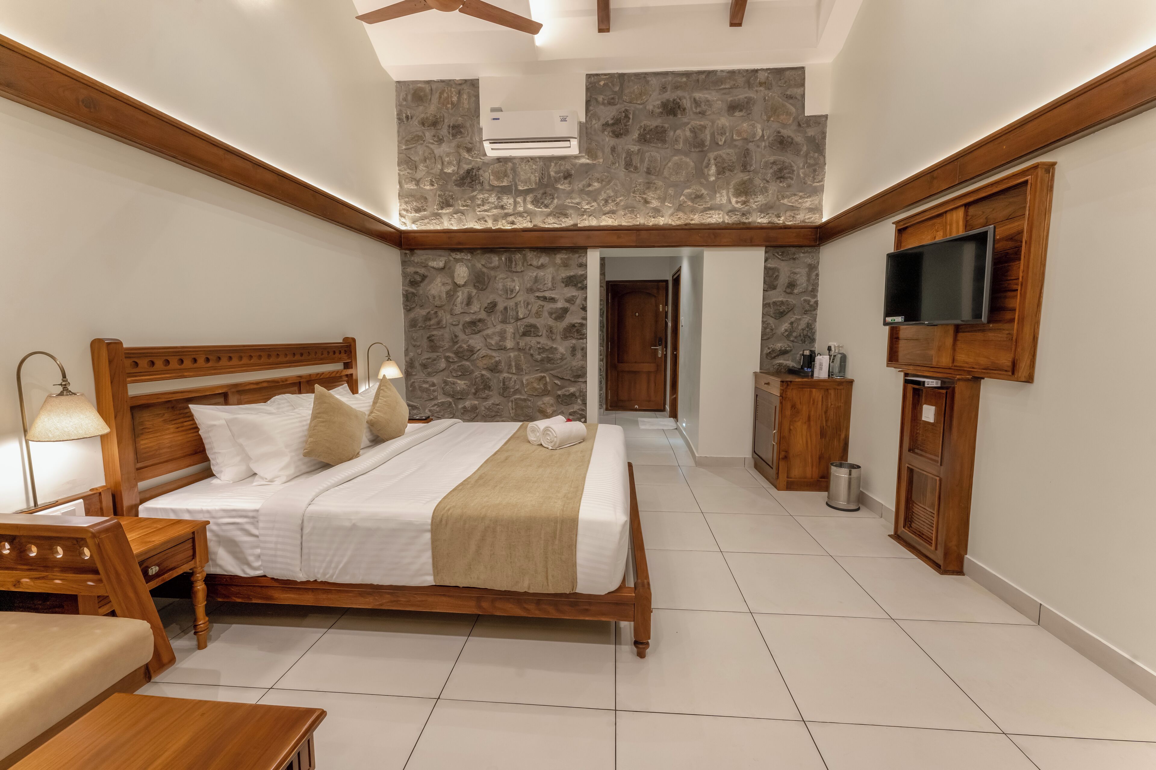 A bedroom with a wooden bed, a TV mounted on the wall, and a stone wall.