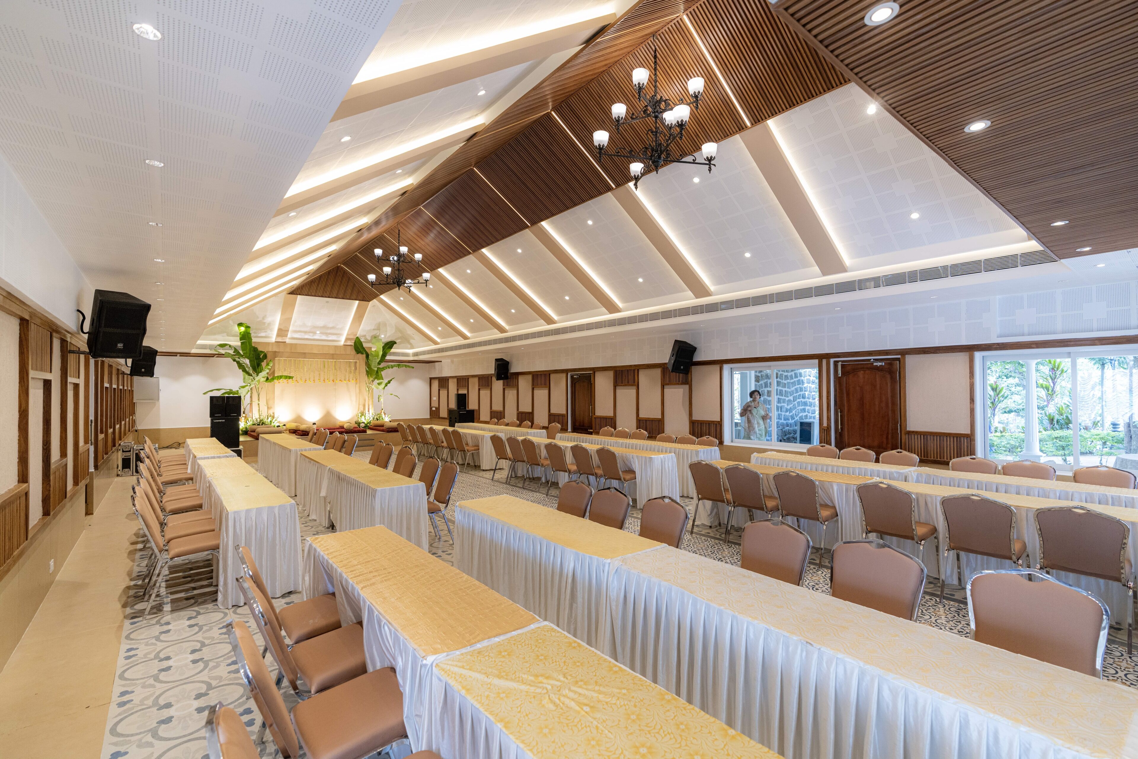 A conference room with long tables, chairs, and a high ceiling with wooden panels and recessed lighting.