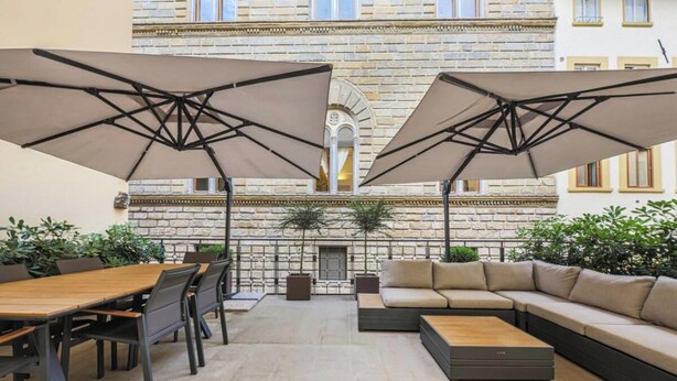 Un patio al aire libre con mesa y sillas de madera, un sofá y dos sombrillas grandes.