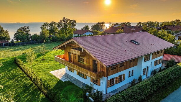 Ein zweistöckiges Holzhaus mit einem Balkon, umgeben von einer gepflegten Rasenfläche und Blick aufs Meer.
