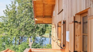 Eine Holzhütte mit Balkon und Blick auf einen See, ausgestattet mit einer Holzterrasse und einem großen Fenster.