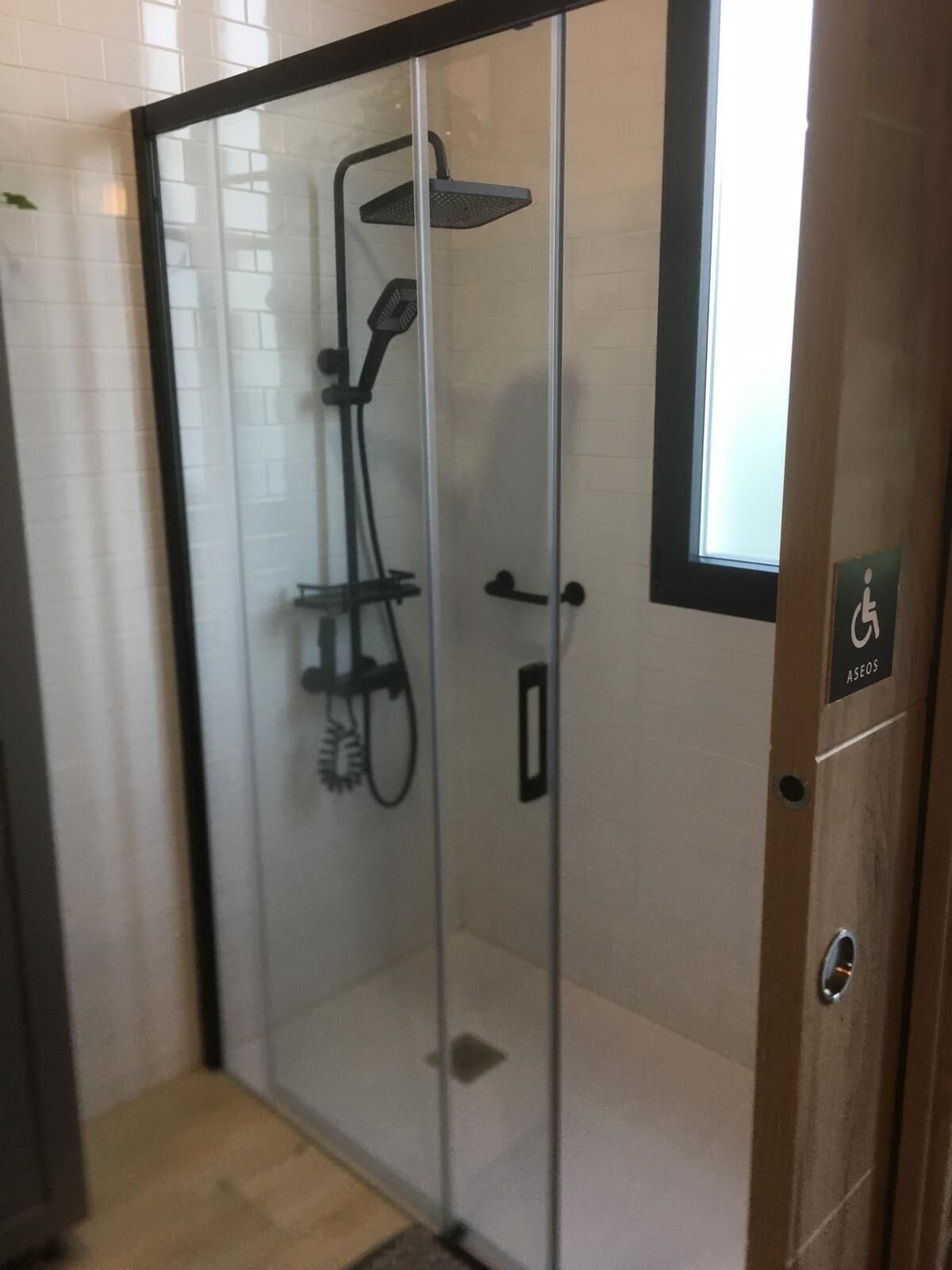 Une cabine de douche fermée par des parois en verre, équipée d’un pommeau de douche à main et d’une brosse à main.