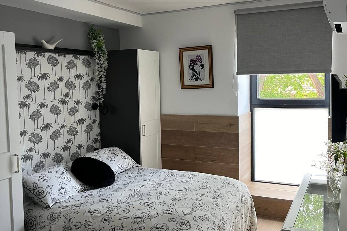 A bedroom with a bed, a desk, a window with a view, and a framed picture on the wall.